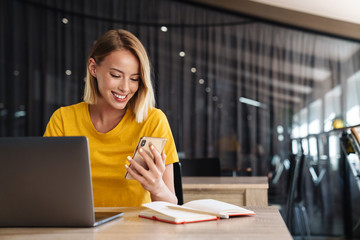 Photo of smiling young woman working on laptop and cellphone