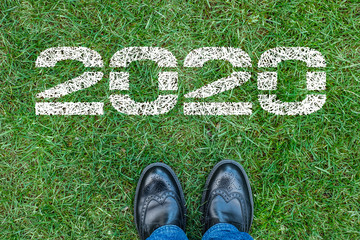 Feet in black boots stand about the figures 2020 on the green grass. Merry Christmas and Happy New 2020 year.