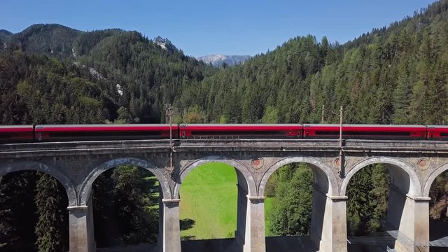 Aerial view of red train rides on famous Kalte Rinne Viaduct on historical Semmering mountain railway (Semmeringbahn), Lower Austria.