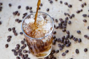 Cold brew coffee pouring into a glass with crushed ice and coffee beans around the glass
