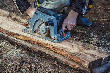 Circular saw for cutting boards into the hands of the builder, the man sawed bars, construction and home renovation, repair and construction tool. Carpenter Using Circular Saw for wood. Close-up