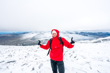 A man/hiker with red jacket and norwegian flag on his chest standing on a snowy mountain peak with...
