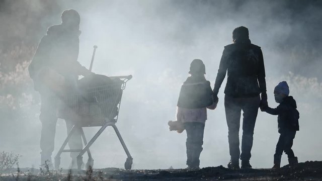 Back view of survivor family in gas mask going through clouds of toxic smoke and cinder in empty dead landscape.