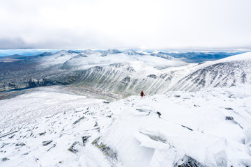 Obraz premium Girl with red hooded jacket and backpack are hiking in snow covered mountains with beautiful scenic landscape view and foggy weather. Scenery, lifestyle, active and outdoor concept.