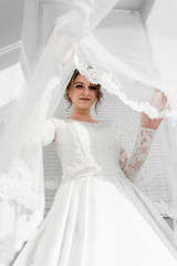 Fototapeta premium Portrait of young gorgeous bride with bridal veil. Wedding day gatherings. Beautiful girl dresses and gathers for a wedding ceremony in apartaments while waiting for the groom. Bride's morning