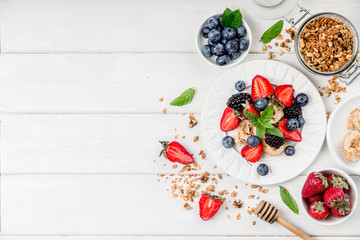 Healthy breakfast with granola, fruits, berries on white background.