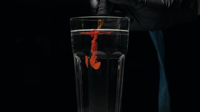 Close-up of tattoo machine cleaning slow is washed with needles in clear water from pigment of red paint.