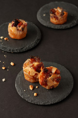 Small mini tarts with raisins and nuts on round black stone board on black in low key.