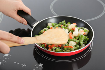 Woman cooking frozen vegetable mix on induction stove, closeup
