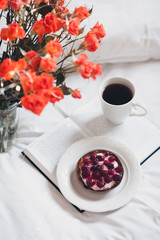 Fruit cake with cup of black tea staying on open book with orange roses in bed closeup. Good morning.