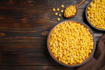 Delicious canned corn in bowl on wooden table, flat lay. Space for text