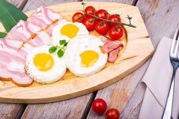 Tasty fried eggs with vegetables on a wooden plate.