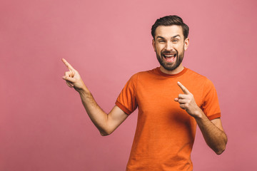 Look over there! Happy young handsome man in casual pointing away and smiling while standing against pink background.