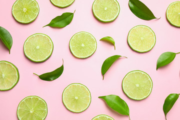 Juicy fresh lime slices and green leaves on pink background, flat lay