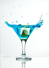 martini glass with blue gin and a slice of lemon, splash and spray on a light background