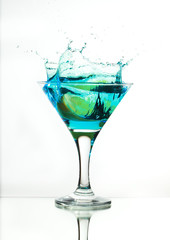 martini glass with blue gin and a slice of lemon, splash and spray on a light background