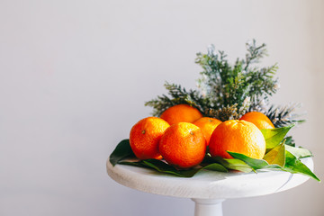 Orange tangerines on grey background in New Year's decor with brown pine cones and green leaves. Christmas decoration with mandarins. Delicious sweet clementine.
