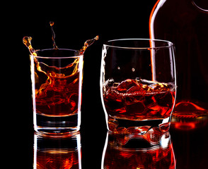 Glass and bottle of whiskey with splash on dark background, selective focus on the glass