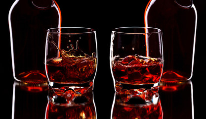 Fototapeta na wymiar Glass and bottle of whiskey with splash on dark background, selective focus on the glass