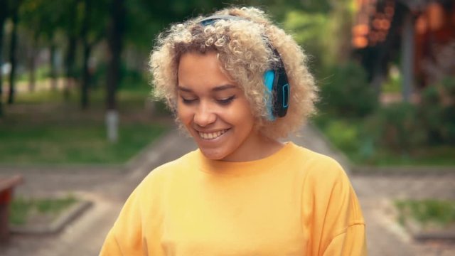 close up portrait happy mixed race young woman listening music dancing walking summer nature in city park slow motion