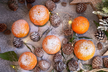 Orange tangerines on grey background in New Year's decor with brown pine cones and green leaves. Christmas decoration with mandarins. Delicious sweet clementine.