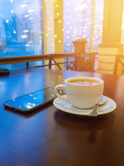 a Cup of green tea on a wooden table in a cafe. the smartphone is nearby. led lights and window in the background. bokeh. Garlands