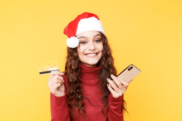 Christmas shopping concept. Cute woman holding phone and credit card in the santa's hat