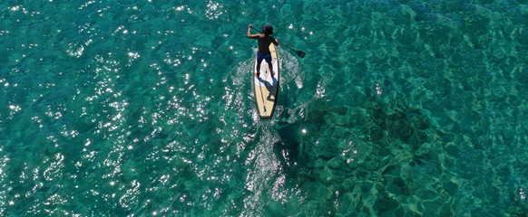 Aerial drone ultra wide panoramic photo of unidentified fit man practising in Stand Up Paddle board or SUP in tropical island exotic turquoise bay
