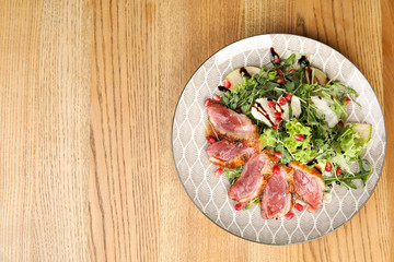 Delicious salad with roasted duck breast served on wooden table, top view. Space for text