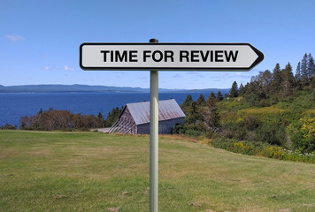Road sign with TIME FOR REVIEW text under countryside background