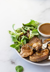 Fried juicy pork chops with caramelized onion and sauce served with green salad and beans. Light grey background, selective focus.