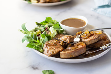 Fried juicy pork chops with caramelized onion and sauce served with green salad and beans. Light grey background, selective focus.