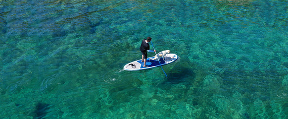 Aerial drone ultra wide panoramic photo of unidentified fit man paddling with his cute dog on a SUP...