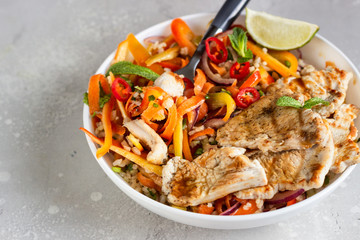 Buddha bowl lunch with grilled chicken and carrot, red bell pepper, onion, rice and herbs on light grey stone background. Healthy balanced eating. Comfort food.