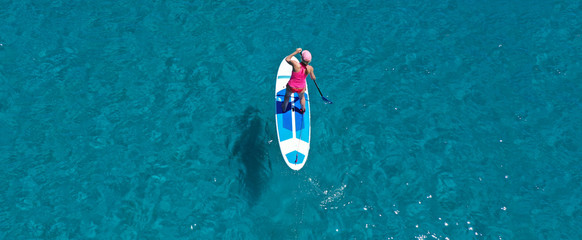 Aerial drone ultra wide panoramic photo of unidentified fit woman practising in Stand Up Paddle board or SUP in tropical island exotic turquoise bay