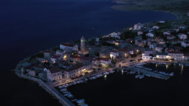 Tranquil village waterfront lit warmly at dusk, advancing aerial