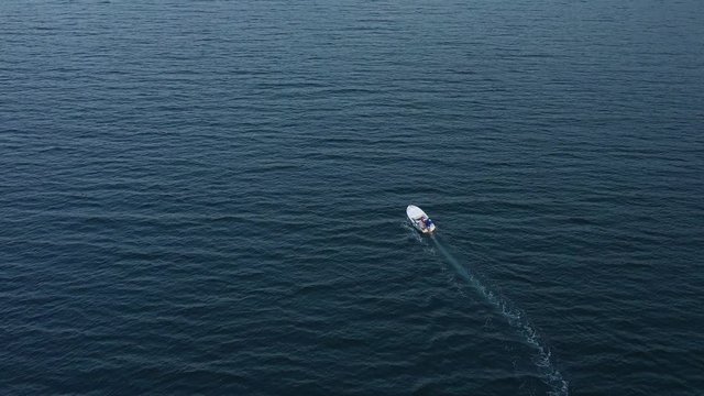 A single small white motorboat crossing wide expanse of sea, aerial