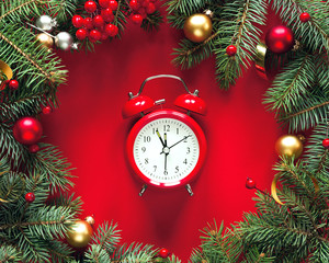 Fototapeta na wymiar Fir branches in holiday decorations and an red vintage alarm clock on a red background, top view. Christmas winter background, Christmas card. 