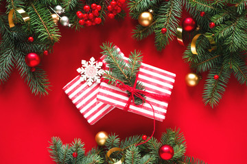 Fir branches, holiday decorations and gift or present boxes on a red background, top view with space for text. Christmas winter background, Christmas card. 	