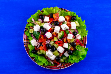 plate of tasty healthy greek salad on a blue table , national dish of Greece on a beautiful background , greek's kitchen with spices , fork and lemon