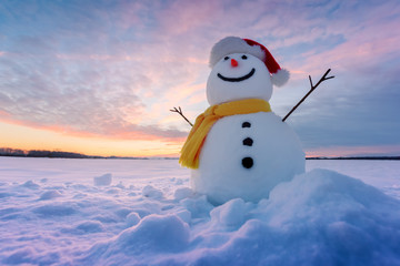 Fototapeta premium Funny snowman in red santa hat and yellow scalf on snowy field. Christmass and New Year background