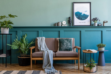 Stylish interior design of living room at apartment with brown sofa, a lot of plants, design furnitures and elegant accessories. Mock up poster frames on the shelf. Green wood panelling. Home staging.