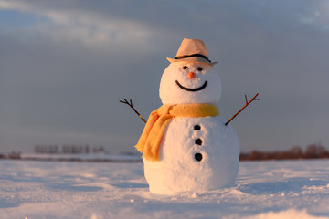 Funny snowman in stylish hat and yellow scalf on snowy field. Merry Christmass and happy New Year!