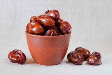Dried fruit dates in a brown bowl on a gray fabric background