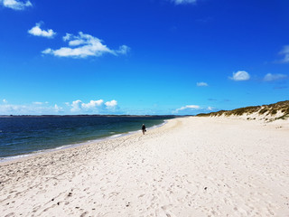 Strand bei List auf der Insel Sylt bei blauen Himmel mit weißen Wolken und einem Spaziergänger in der Ferne