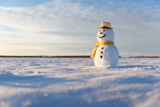 Funny snowman in stylish hat and yellow scalf on snowy field. Merry Christmass and happy New Year!