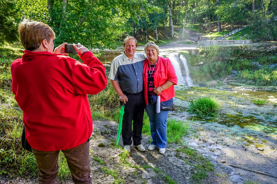 Mature tourists walk and take pictures in the Park at the waterfall