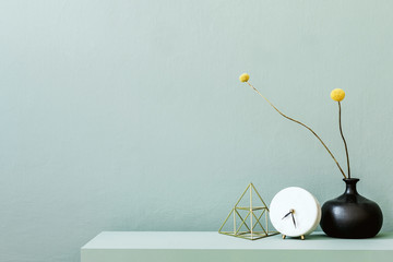 Minimalistic interior design of living room at nice apartment with stylish shelf, vase with flowers, gold pyramid, clock and elegant accessories. Copy space. Eucalyptus color concept. Template.