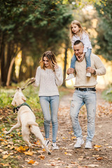 Fototapeta premium Happy beautiful family with dog labrador is having fun together walking the in park.