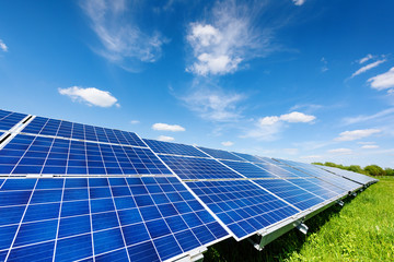 Solar panel on blue sky background. Green grass and cloudy sky. Alternative energy concept